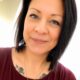 Professional headshot of Christian life coach minister Amberroysa wearing a cross necklace and burgundy top.