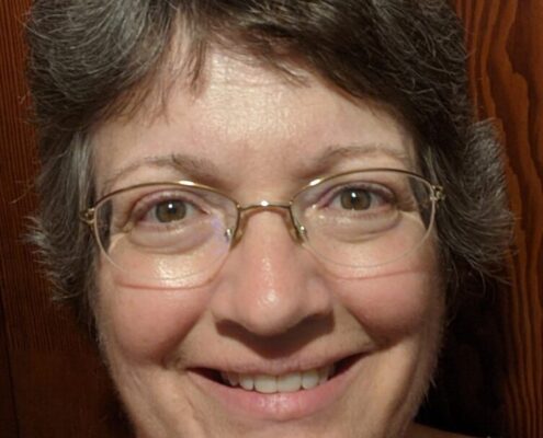 Professional headshot of Christian life coach minister Elizabeth smiling while wearing glasses against a wood-paneled background.