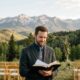 Male Christian wedding officiant standing in the Colorado Rocky Mountains holding an open Bible while preparing to lead a wedding ceremony, representing study-based ordination and Christian wedding ministry in Colorado.