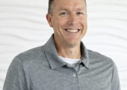 A smiling man in a gray polo shirt poses against a light, neutral background.