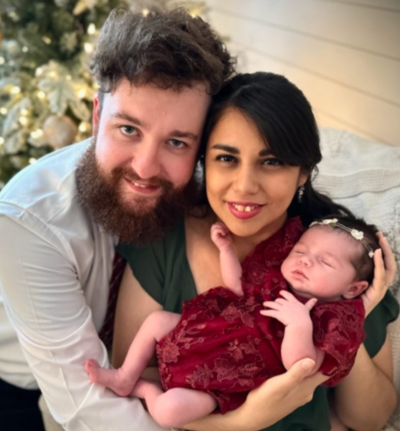 Christian family portrait of parents holding their newborn child in a warm, celebratory setting