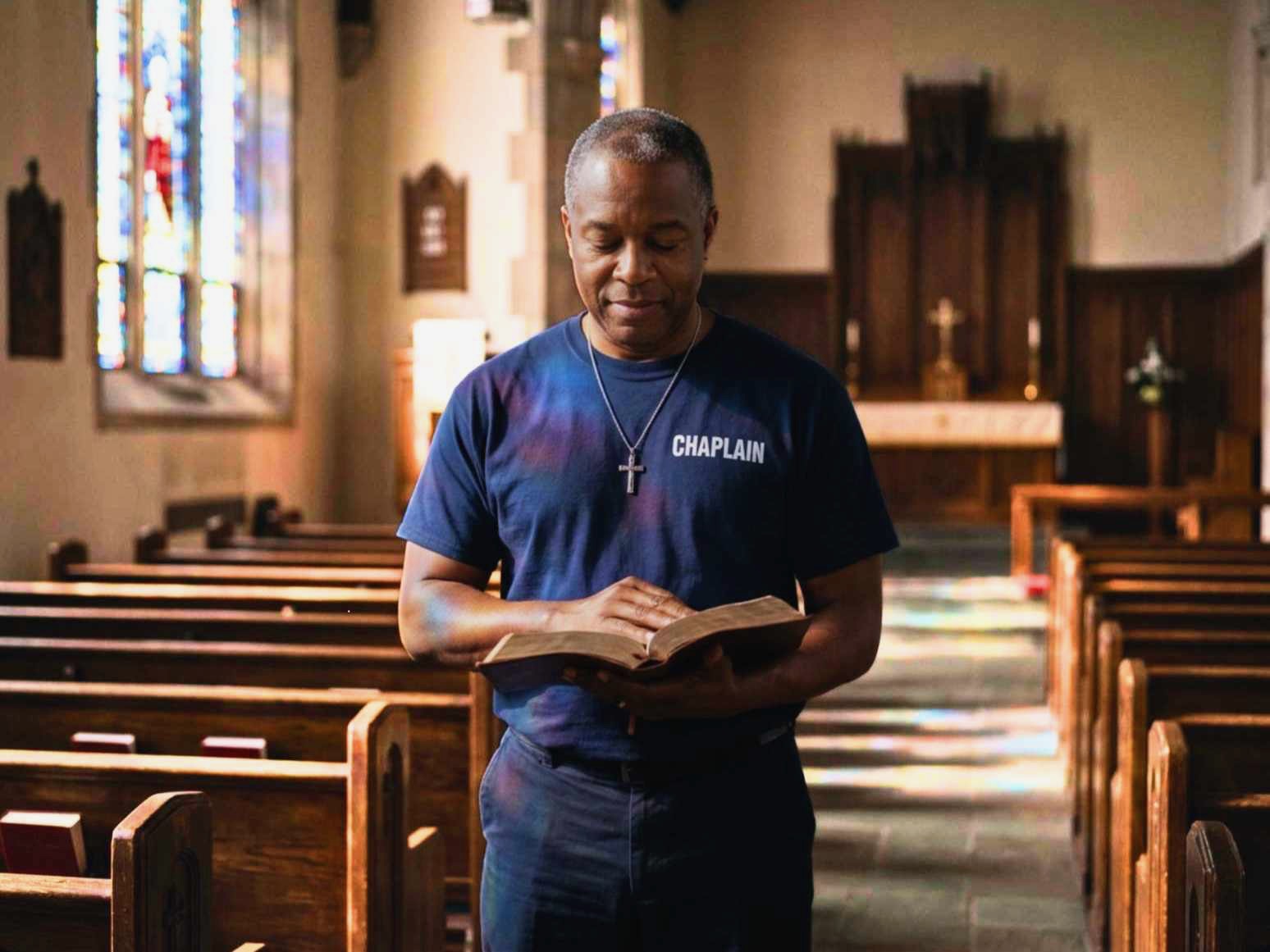 Male chaplain wearing CHAPLAIN shirt praying while holding Bible.