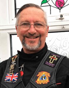 Motorcycle community chaplain wearing a Christian biker vest and smiling while serving bikers through faith-based encouragement and chaplain ministry.
