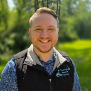 Professional headshot of Austin B., a Christian Life Coach Minister, smiling outdoors while wearing a Springfield Rescue Mission vest.