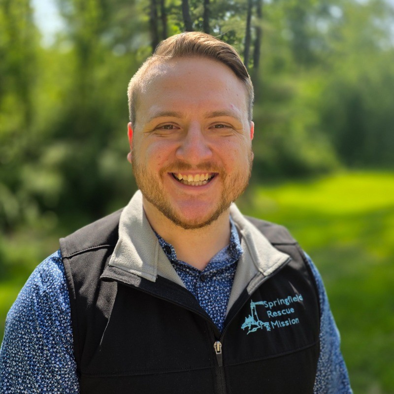 Professional headshot of Austin B., a Christian Life Coach Minister, smiling outdoors while wearing a Springfield Rescue Mission vest.