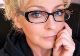Portrait of Christian life coach minister Nicholle S. wearing black glasses and a black top, smiling gently in a professional headshot.